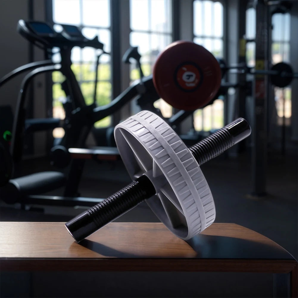 AB Roller Wheel Placed on a Desk with Gym Equipment Blurred in the Background for Core Strength Training and Home Workout